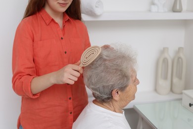 Photo of Granddaughter brushing her grandmother with brush at home, closeup