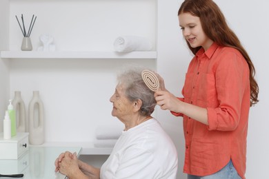 Photo of Granddaughter brushing her grandmother with brush at home