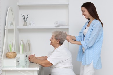 Photo of Woman brushing senior lady with brush indoors