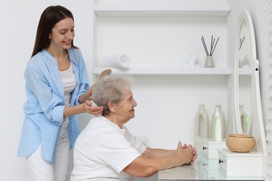 Photo of Woman brushing senior lady with brush indoors