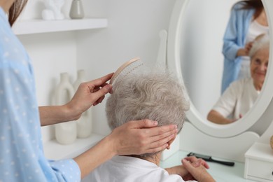 Photo of Woman brushing senior lady with brush indoors, closeup