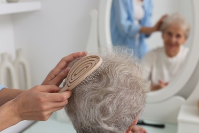 Photo of Woman brushing senior lady with brush indoors, closeup