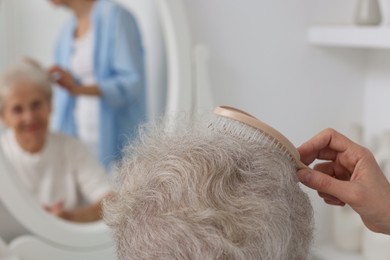 Photo of Woman brushing senior lady with brush indoors, closeup