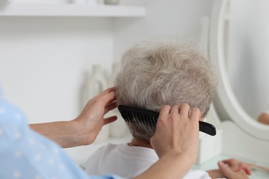 Photo of Woman brushing senior lady with comb indoors, closeup