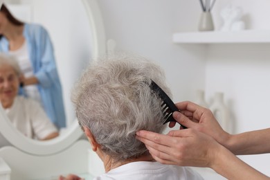 Photo of Woman brushing senior lady with comb indoors, closeup