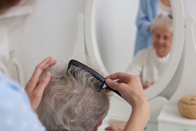 Photo of Woman brushing senior lady with comb indoors, closeup