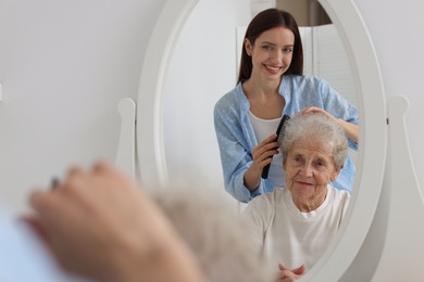 Photo of Woman brushing senior lady with comb indoors