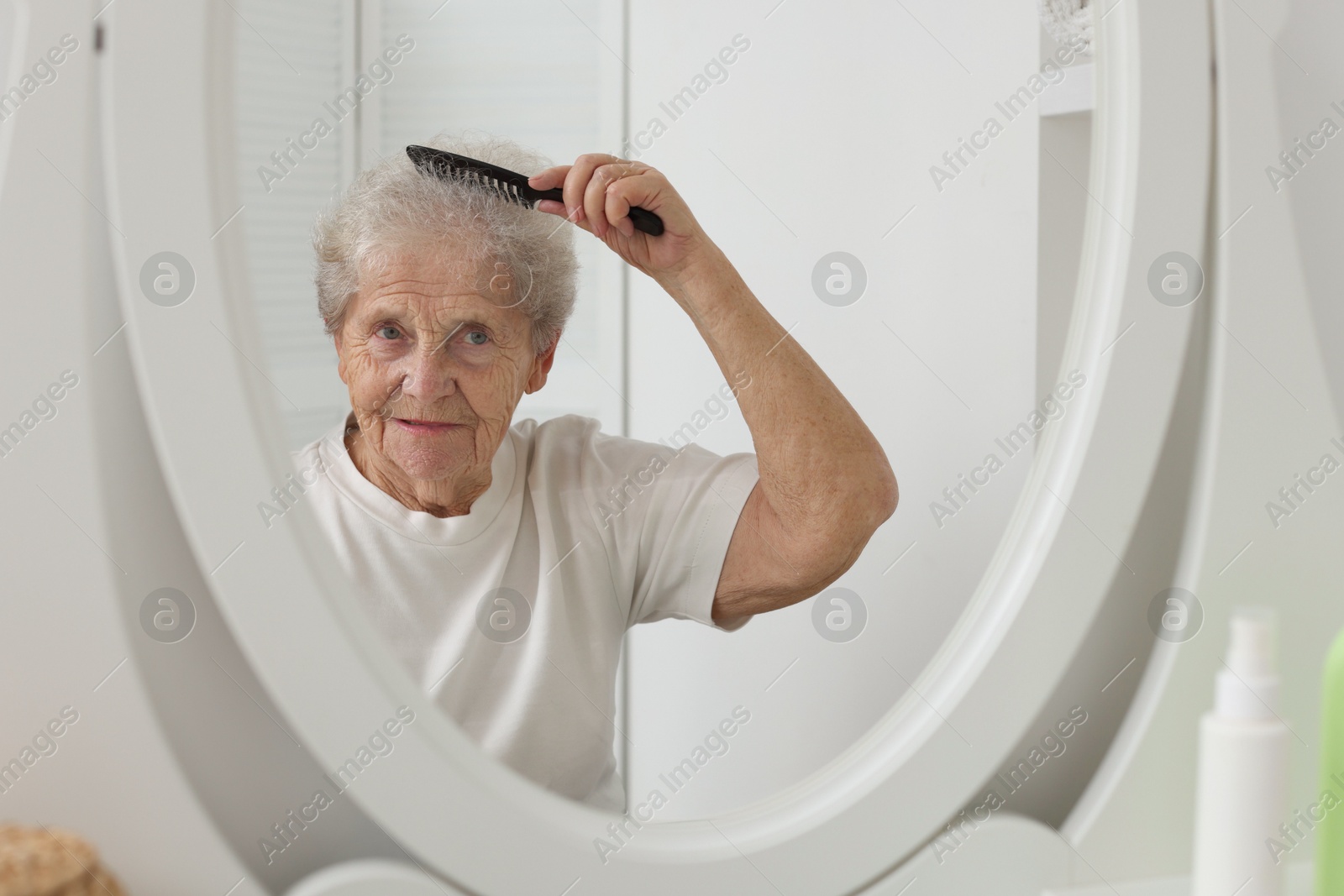 Photo of Senior woman brushing her hair with comb near mirror indoors