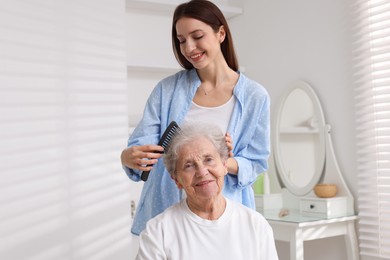 Photo of Beautiful woman brushing senior lady at home