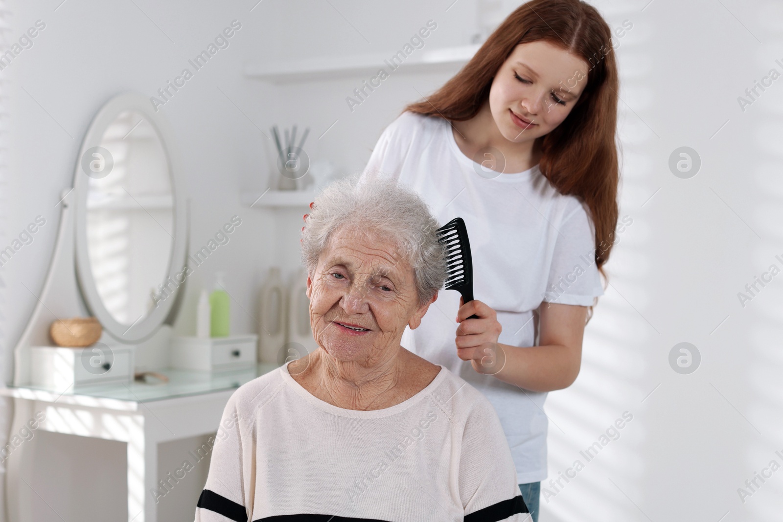 Photo of Granddaughter brushing her grandmother with comb at home