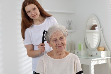 Photo of Granddaughter brushing her grandmother with comb at home