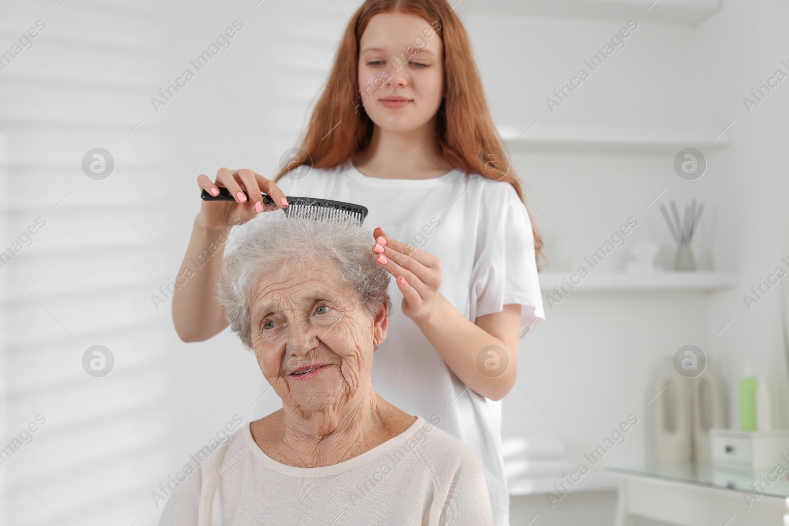 Photo of Granddaughter brushing her grandmother with comb at home