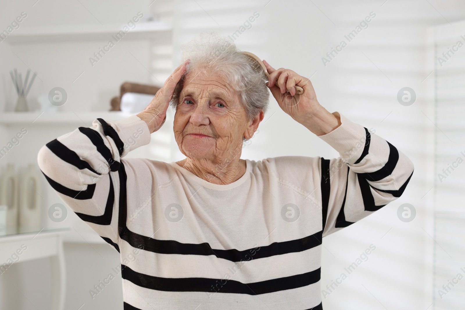 Photo of Senior woman brushing her hair with brush at home