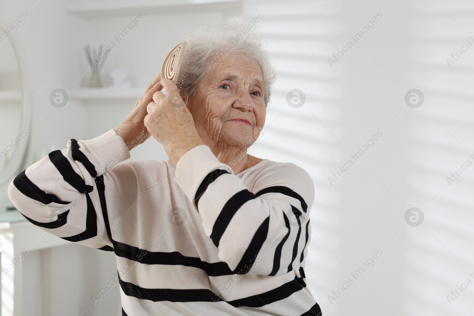 Photo of Senior woman brushing her hair with brush at home, space for text