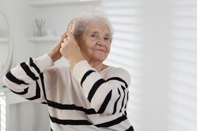 Photo of Senior woman brushing her hair with brush at home, space for text