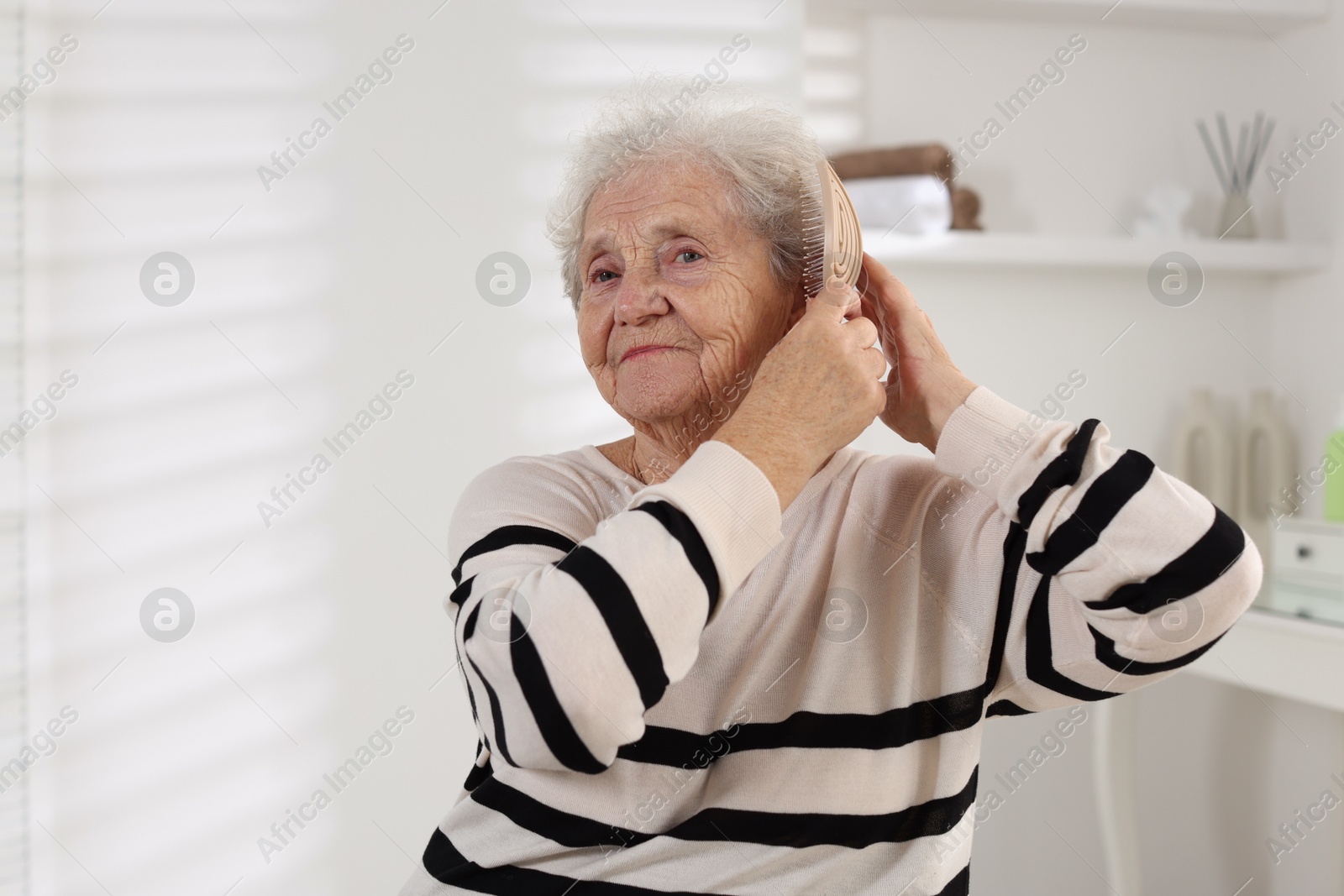 Photo of Senior woman brushing her hair with brush at home, space for text