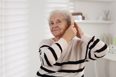 Photo of Senior woman brushing her hair with brush at home, space for text