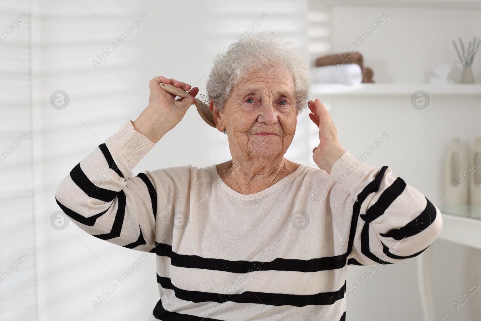 Photo of Senior woman brushing her hair with brush at home