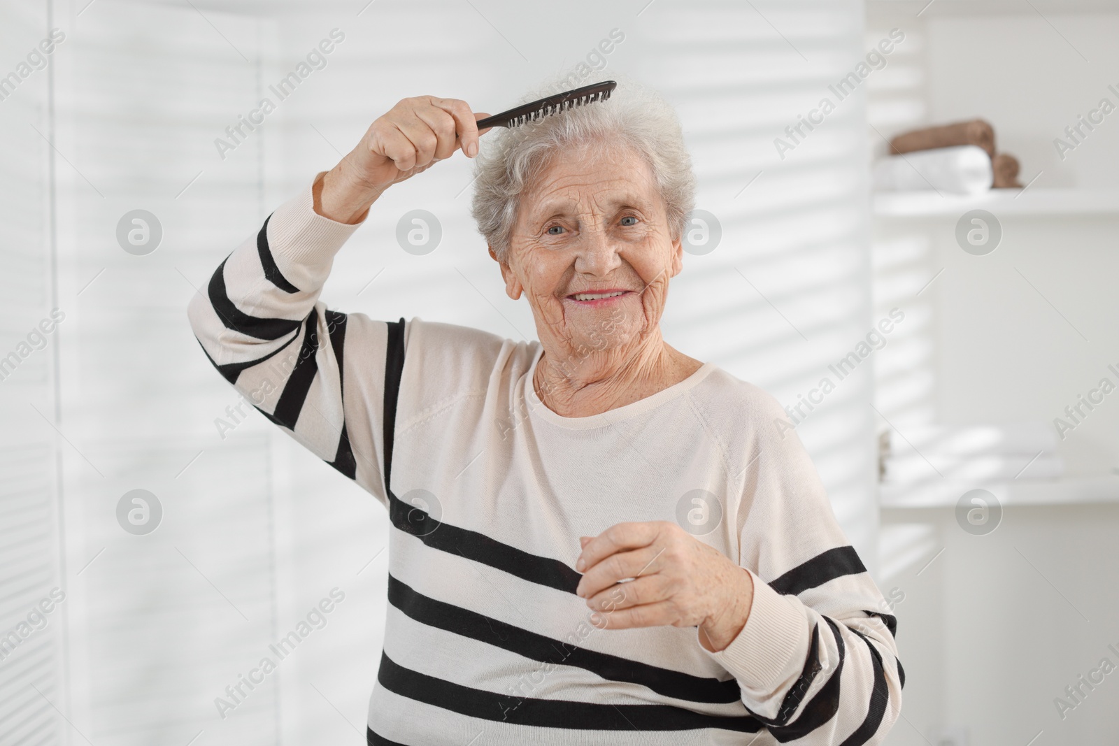 Photo of Senior woman brushing her hair with comb at home