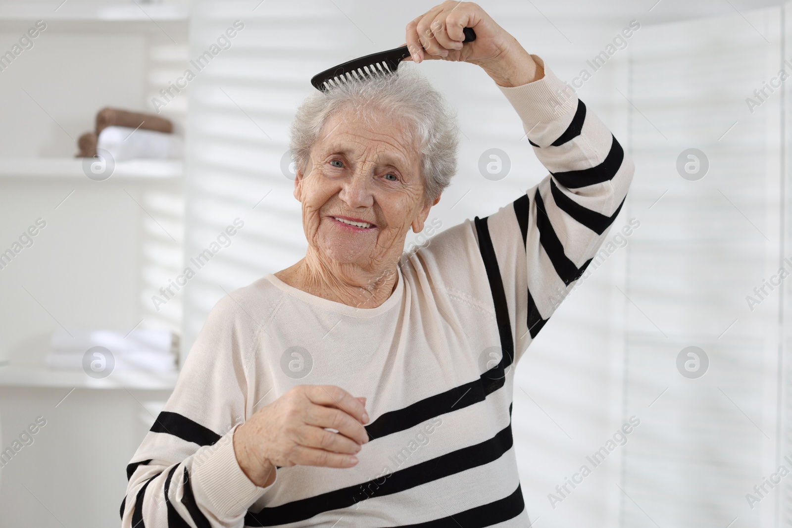 Photo of Senior woman brushing her hair with comb at home