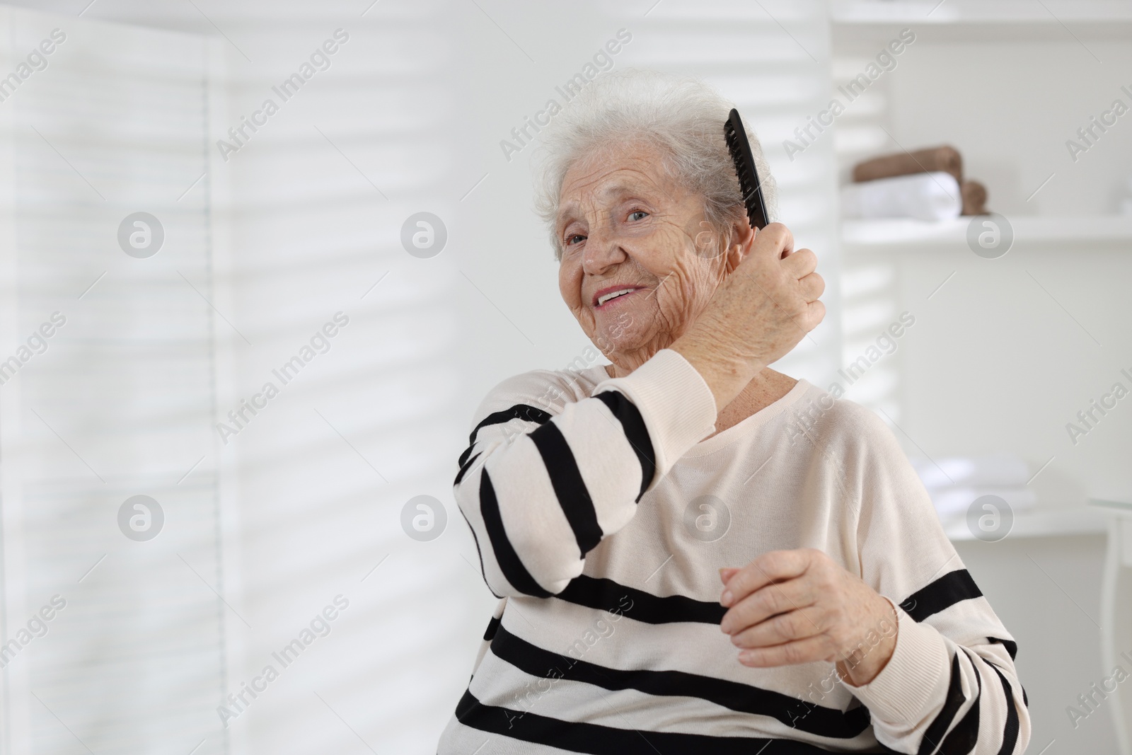 Photo of Senior woman brushing her hair with comb at home, space for text