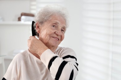 Photo of Senior woman brushing her hair with comb at home, space for text