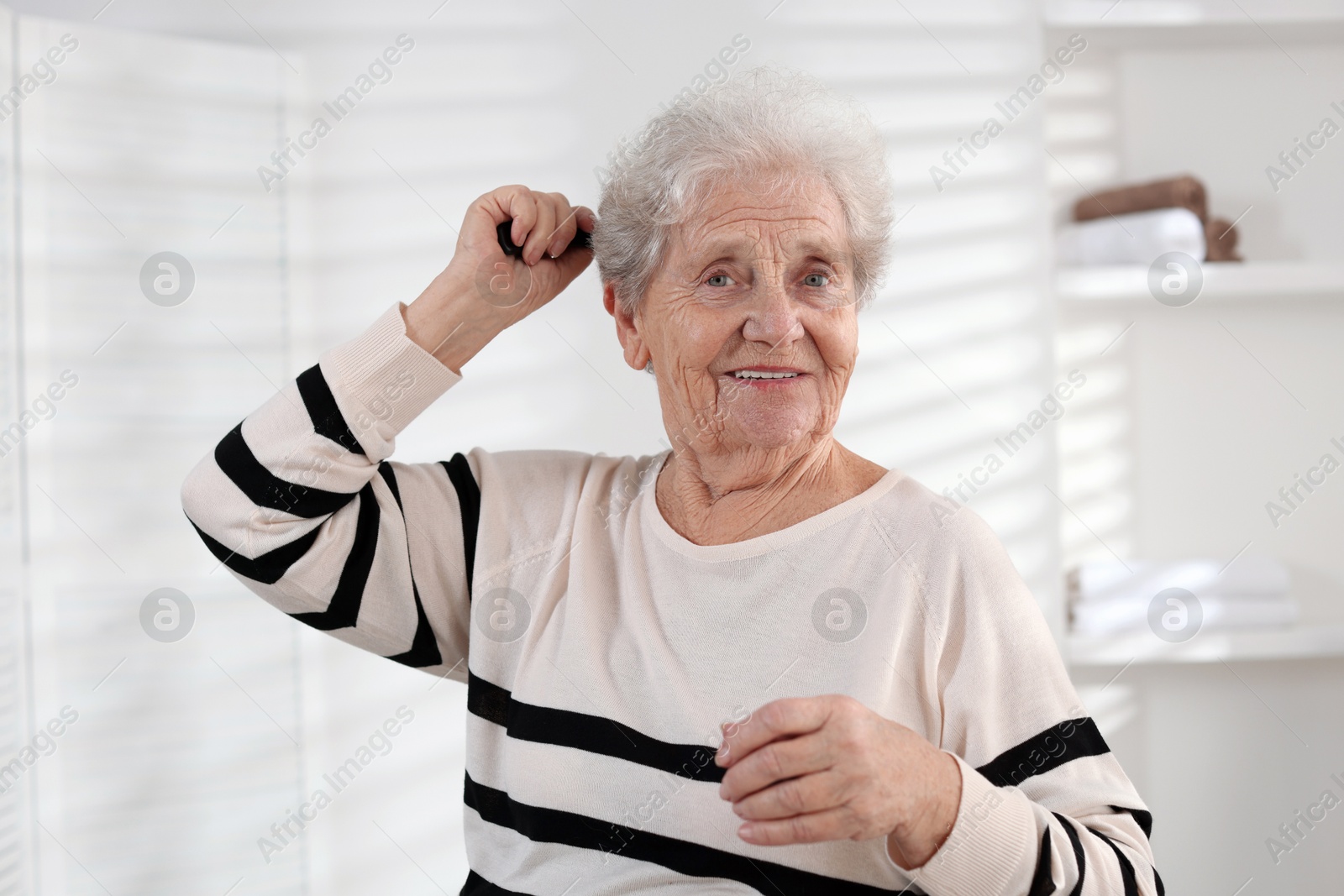 Photo of Senior woman brushing her hair with comb at home