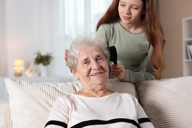 Photo of Granddaughter brushing her grandmother with comb at home