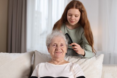 Photo of Granddaughter brushing her grandmother with comb at home