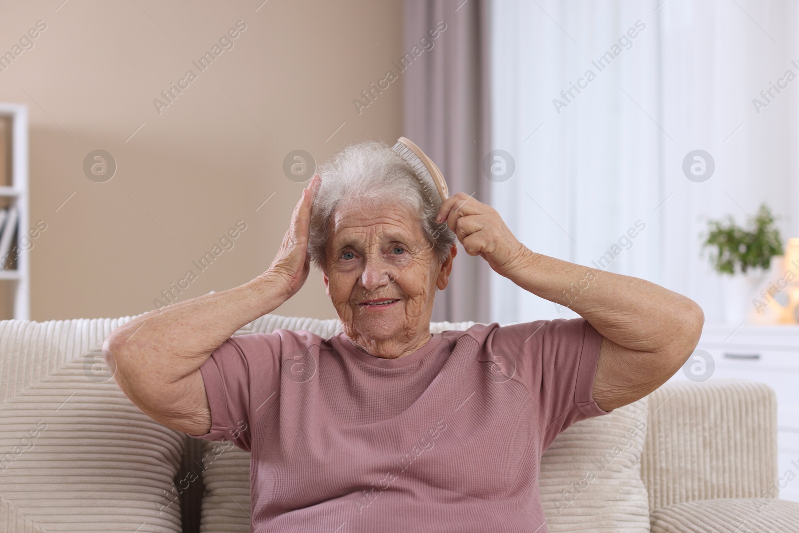 Photo of Senior woman brushing her hair with brush on sofa at home