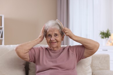 Photo of Senior woman brushing her hair with brush on sofa at home