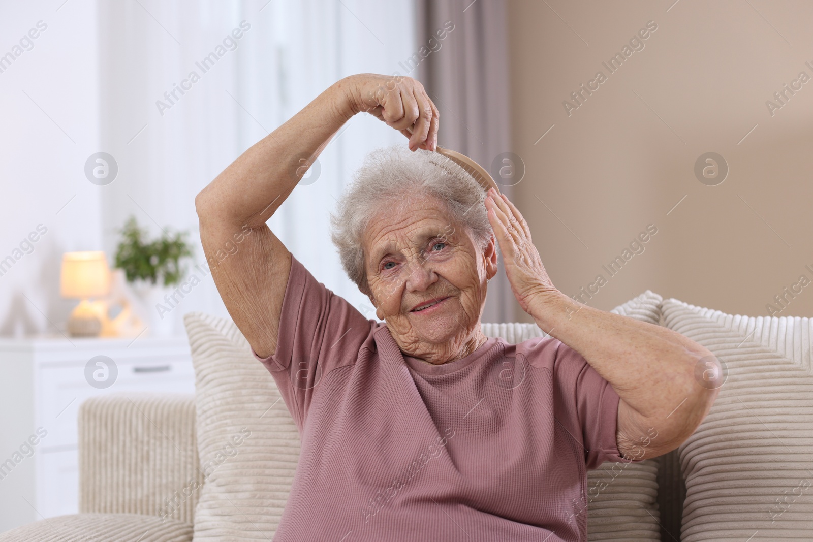 Photo of Senior woman brushing her hair with brush on sofa at home