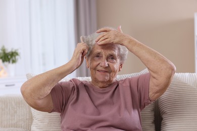 Photo of Senior woman brushing her hair with brush on sofa at home