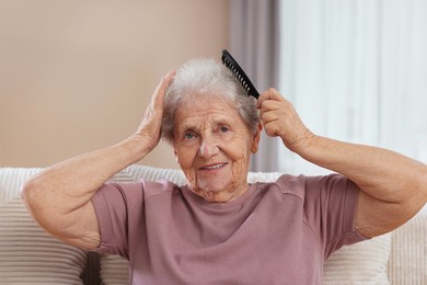 Photo of Senior woman brushing her hair with comb on sofa at home