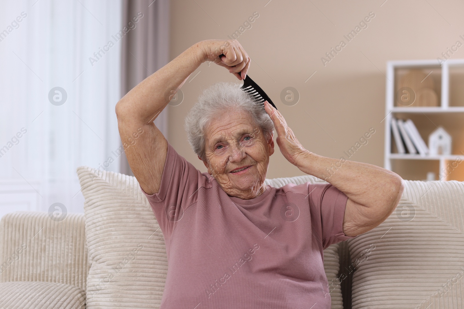 Photo of Senior woman brushing her hair with comb on sofa at home