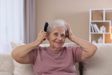 Photo of Senior woman brushing her hair with comb on sofa at home