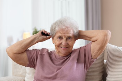 Photo of Senior woman brushing her hair with comb on sofa at home