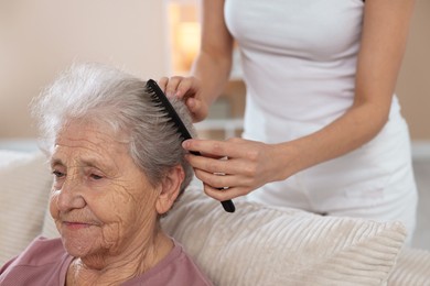 Photo of Woman brushing senior lady with comb indoors, closeup