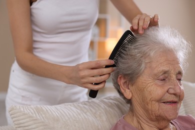 Photo of Woman brushing senior lady with comb indoors, closeup