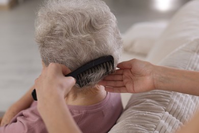 Photo of Woman brushing senior lady with comb indoors, closeup