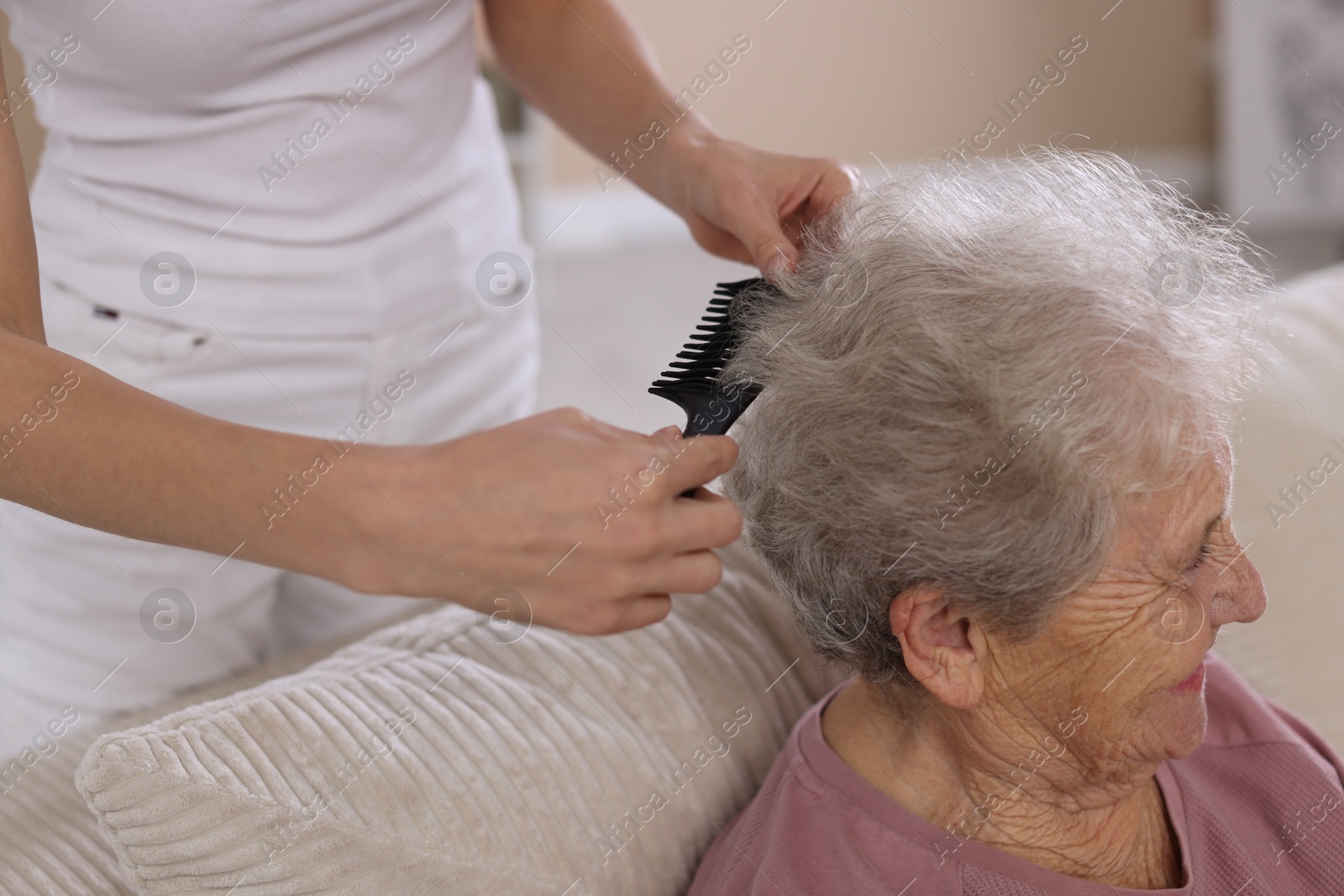 Photo of Woman brushing senior lady with comb indoors, closeup