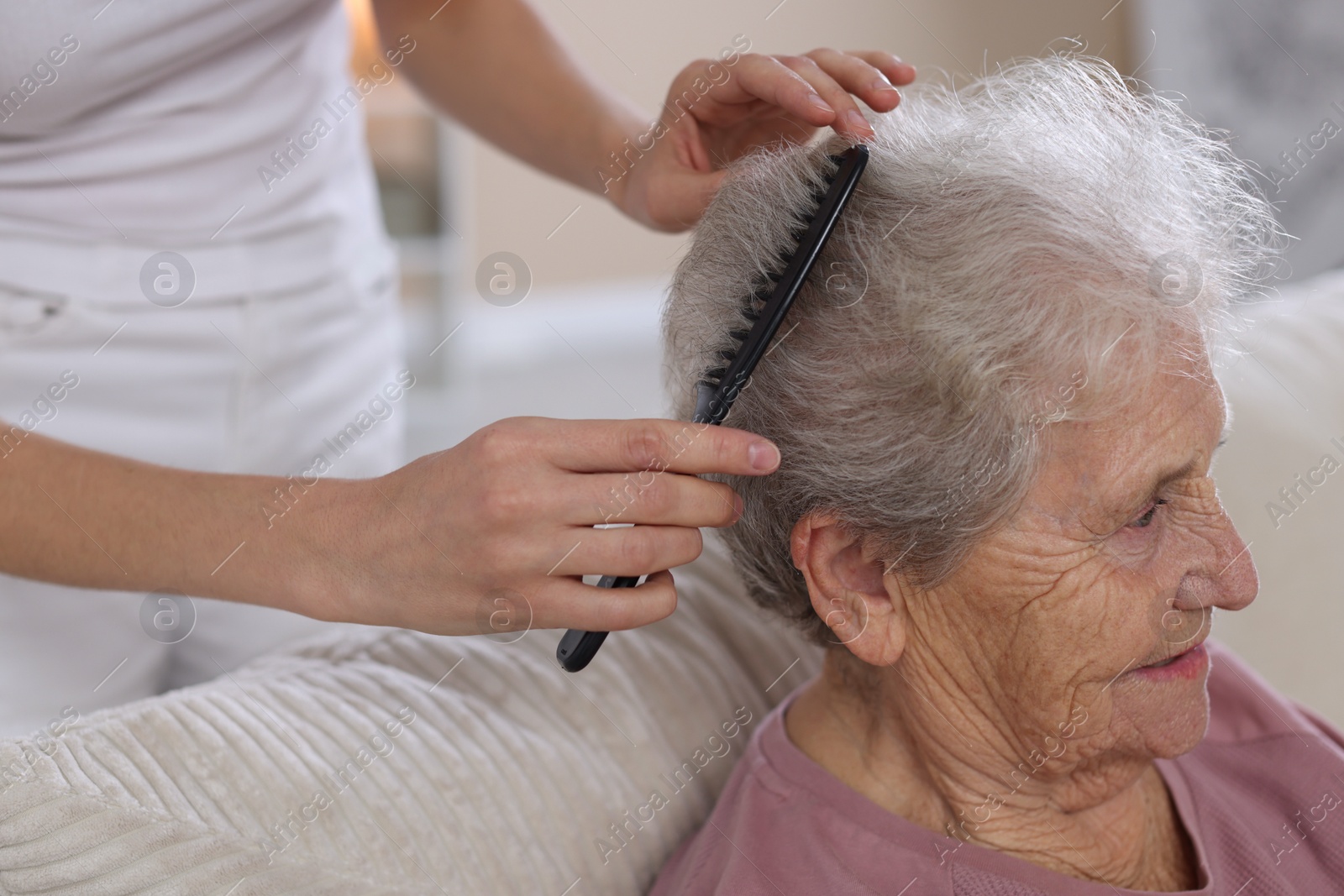 Photo of Woman brushing senior lady with comb indoors, closeup