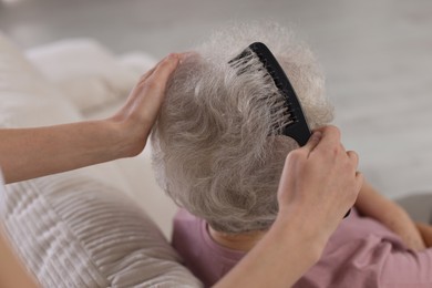 Photo of Woman brushing senior lady with comb indoors, closeup