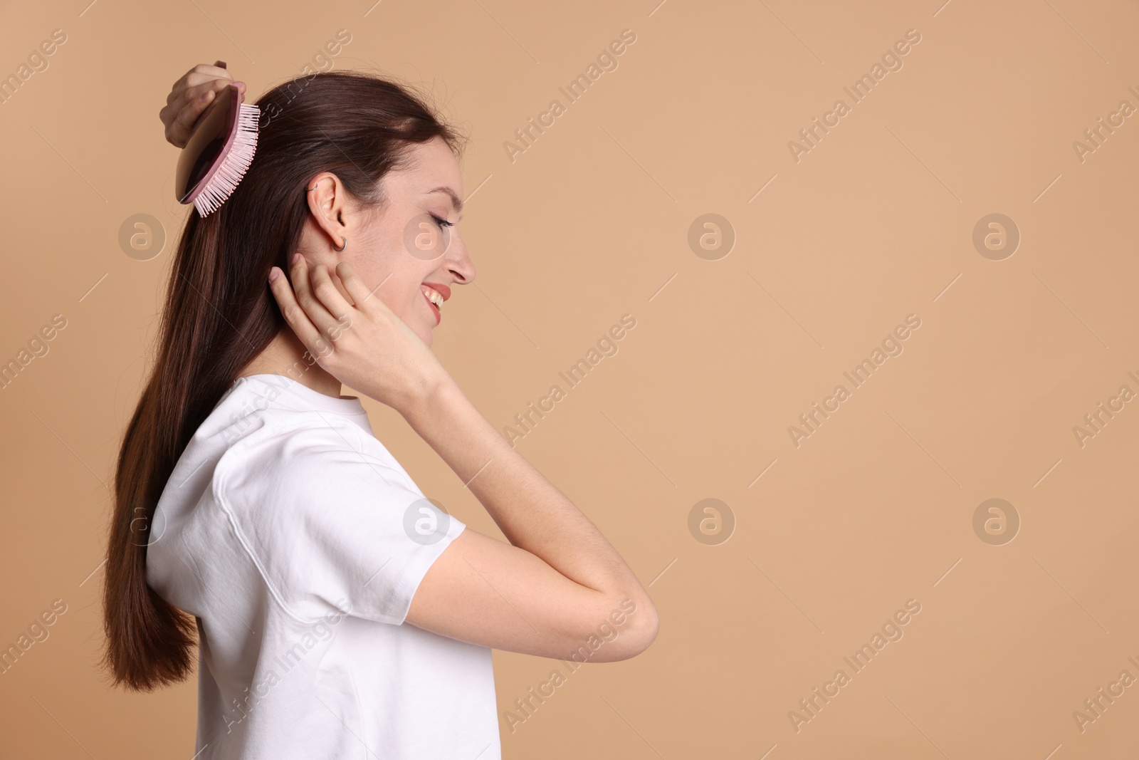 Photo of Smiling woman brushing her hair on beige background, space for text