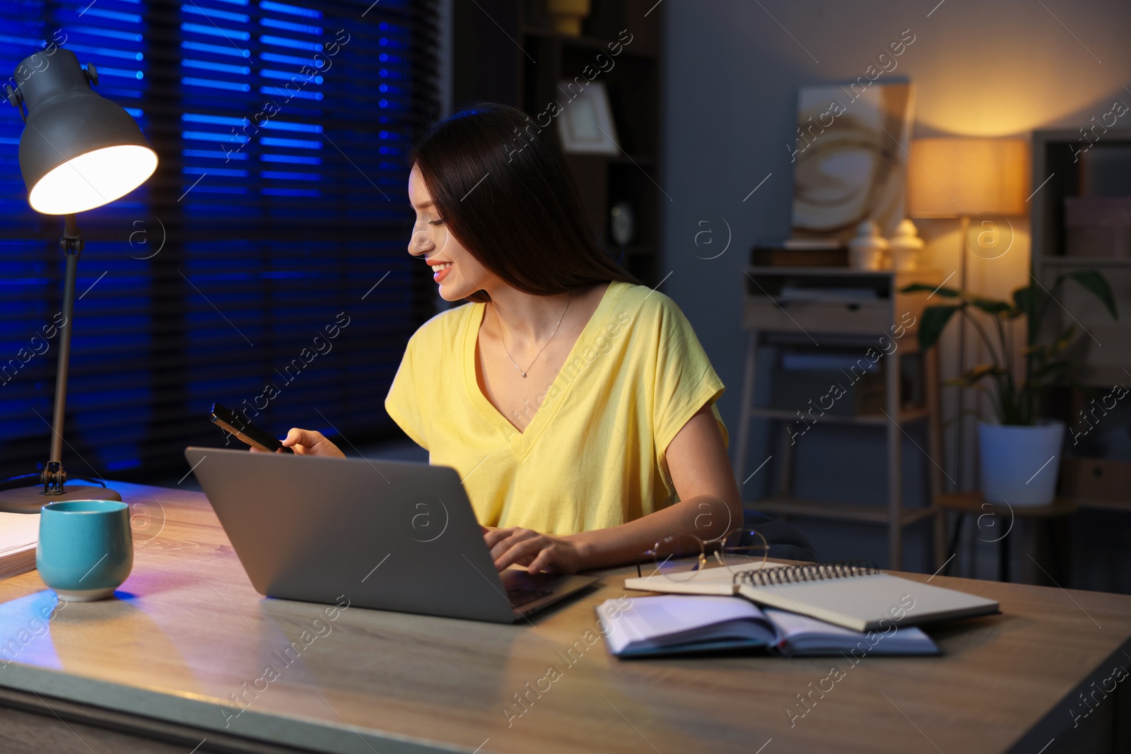 Photo of Woman with smartphone working on laptop at desk in home office