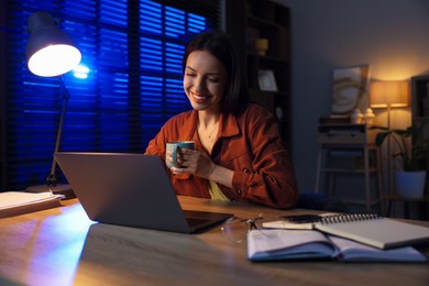 Photo of Woman with cup of coffee working on laptop at desk in home office