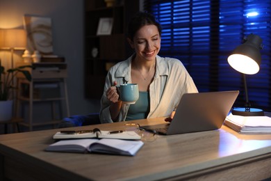 Photo of Woman with cup of coffee working on laptop at desk in home office