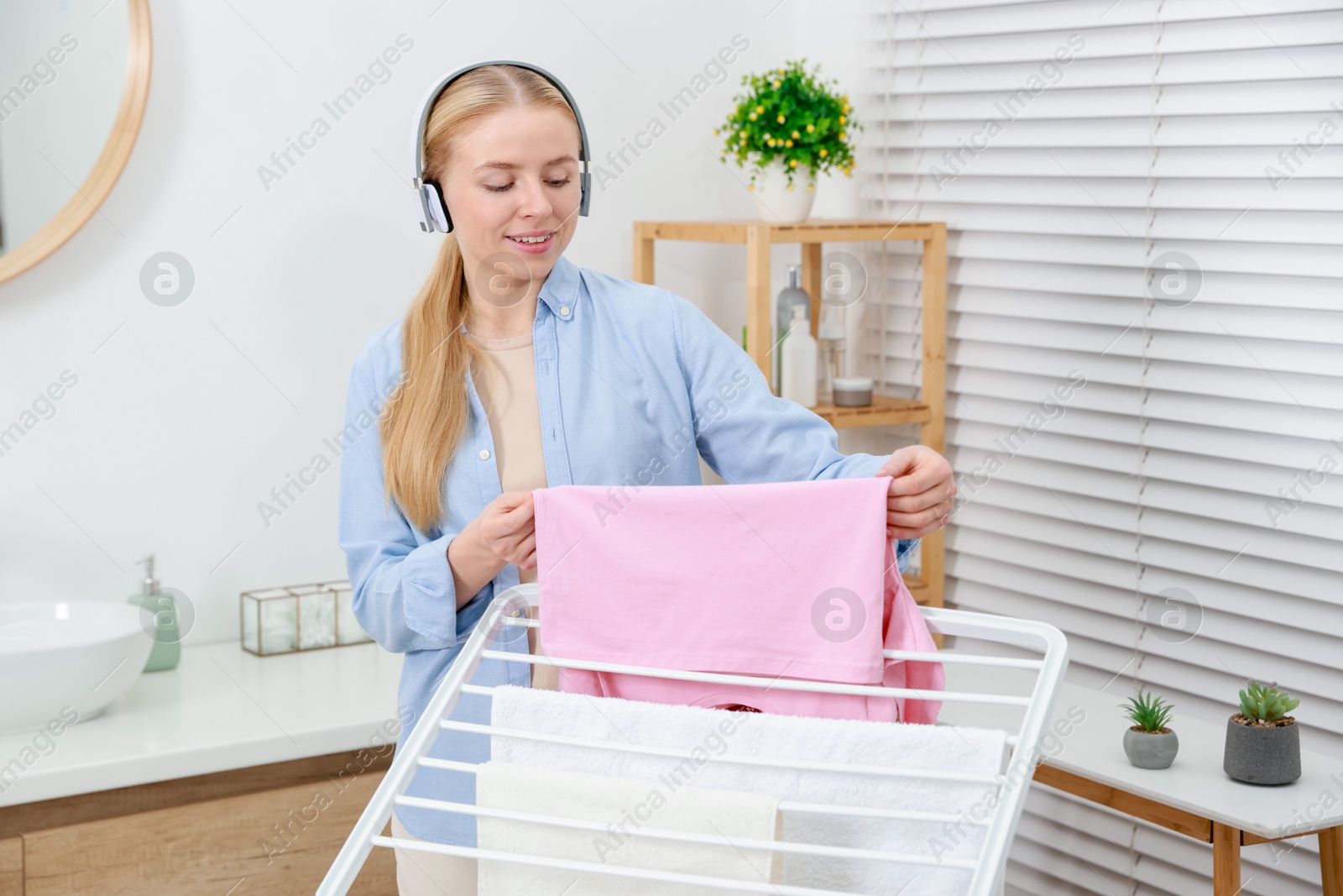 Photo of Woman listening to music while hanging fresh laundry on drying rack at home