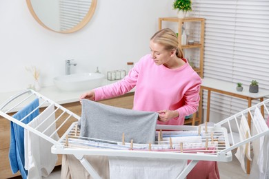 Photo of Beautiful woman hanging fresh clean laundry on drying rack at home