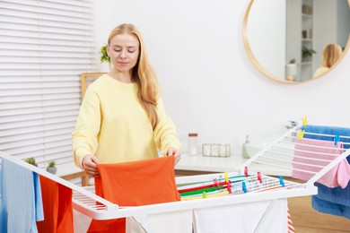 Photo of Beautiful woman hanging fresh clean laundry on drying rack at home